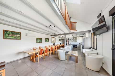 Grande salle à manger du gîte Jonquille avec table pour 15 personnes, plafond bois et cuisine ouverte