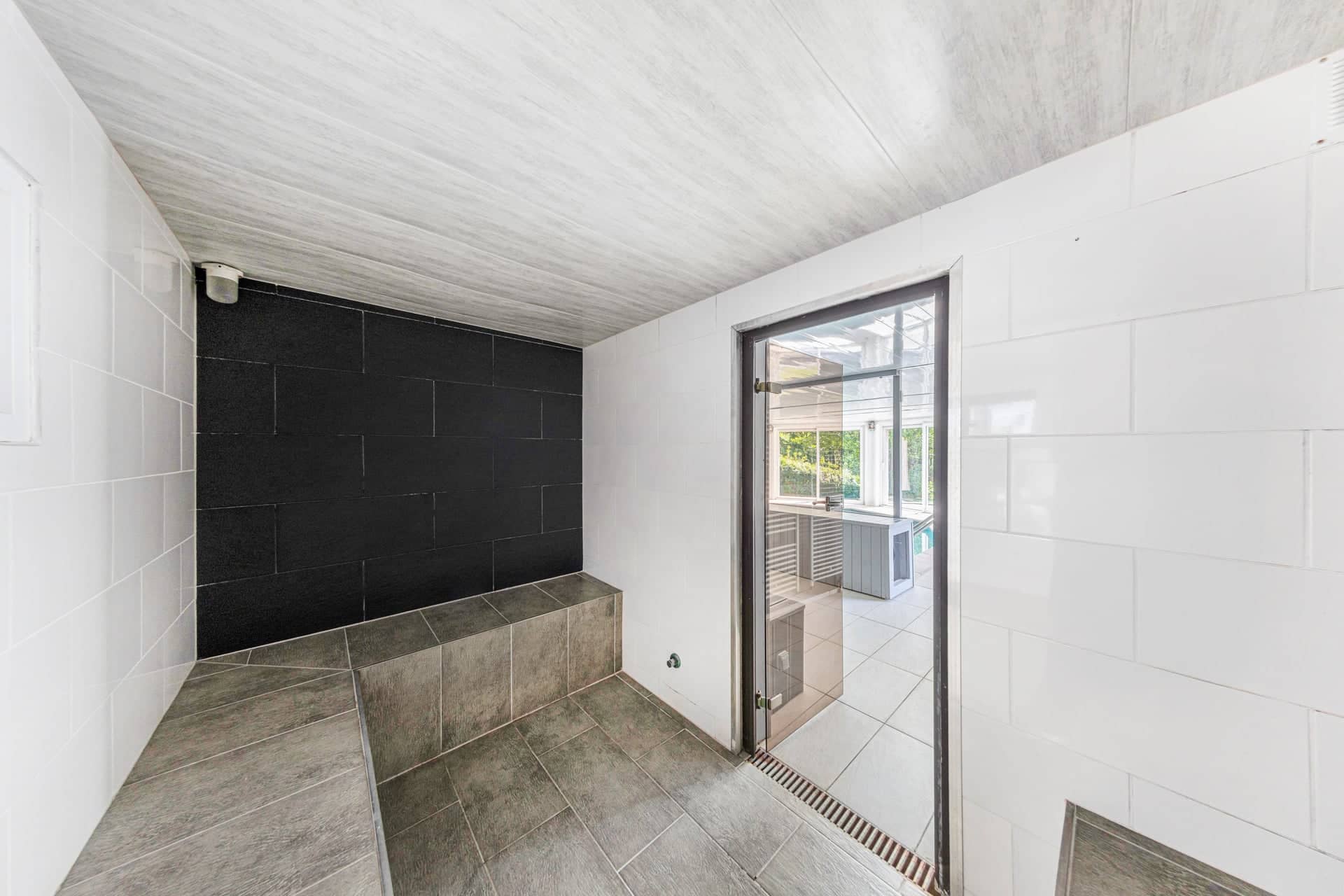 Hammam du gîte Gentiane carrelé noir et blanc avec banc et porte vitrée vers l'espace piscine (gîte groupe avec spa, Alsace)