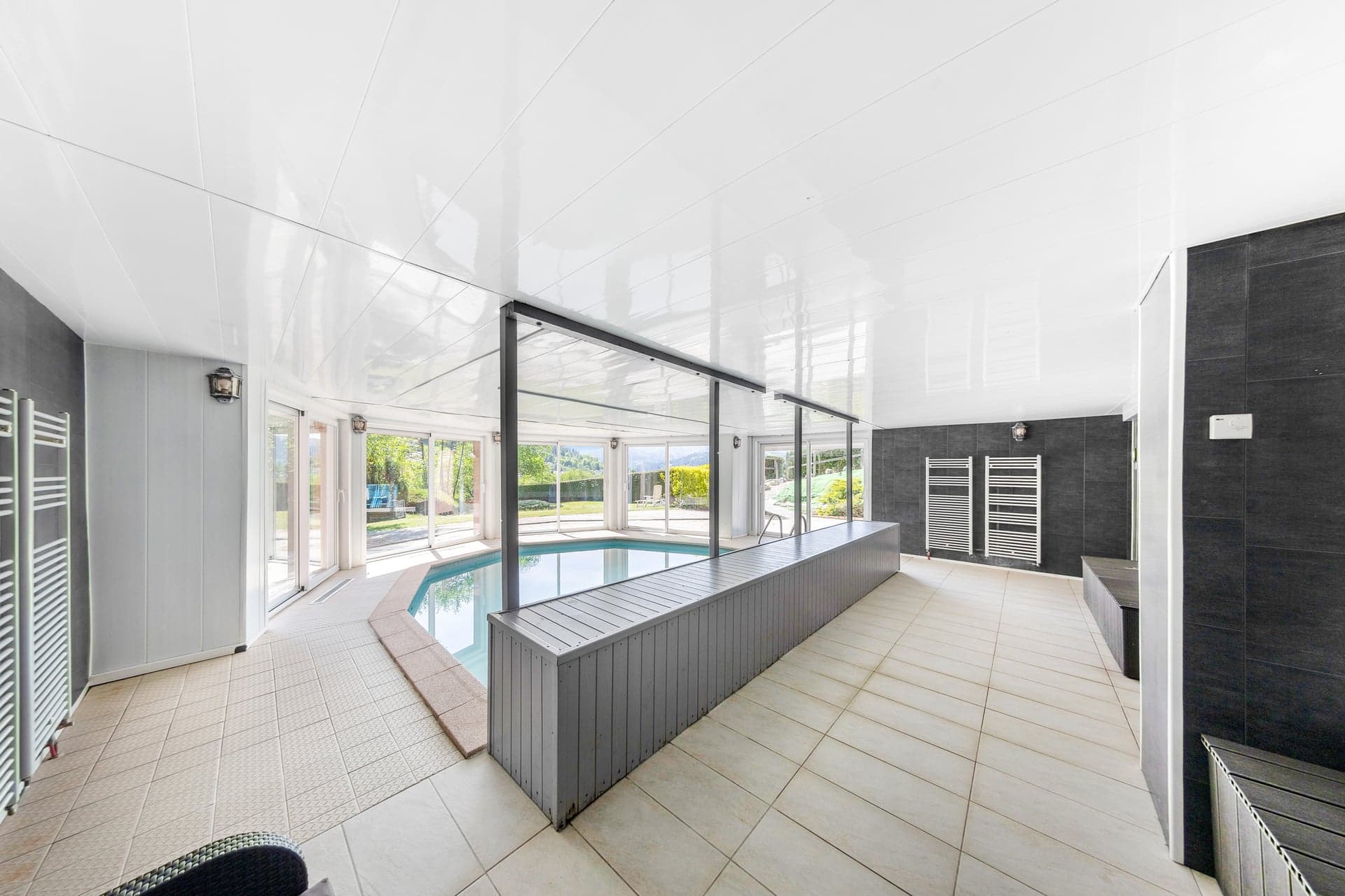 Espace piscine du gîte Gentiane vu depuis le couloir avec baie vitrée panoramique (gîte avec piscine couverte, Hautes-Vosges)