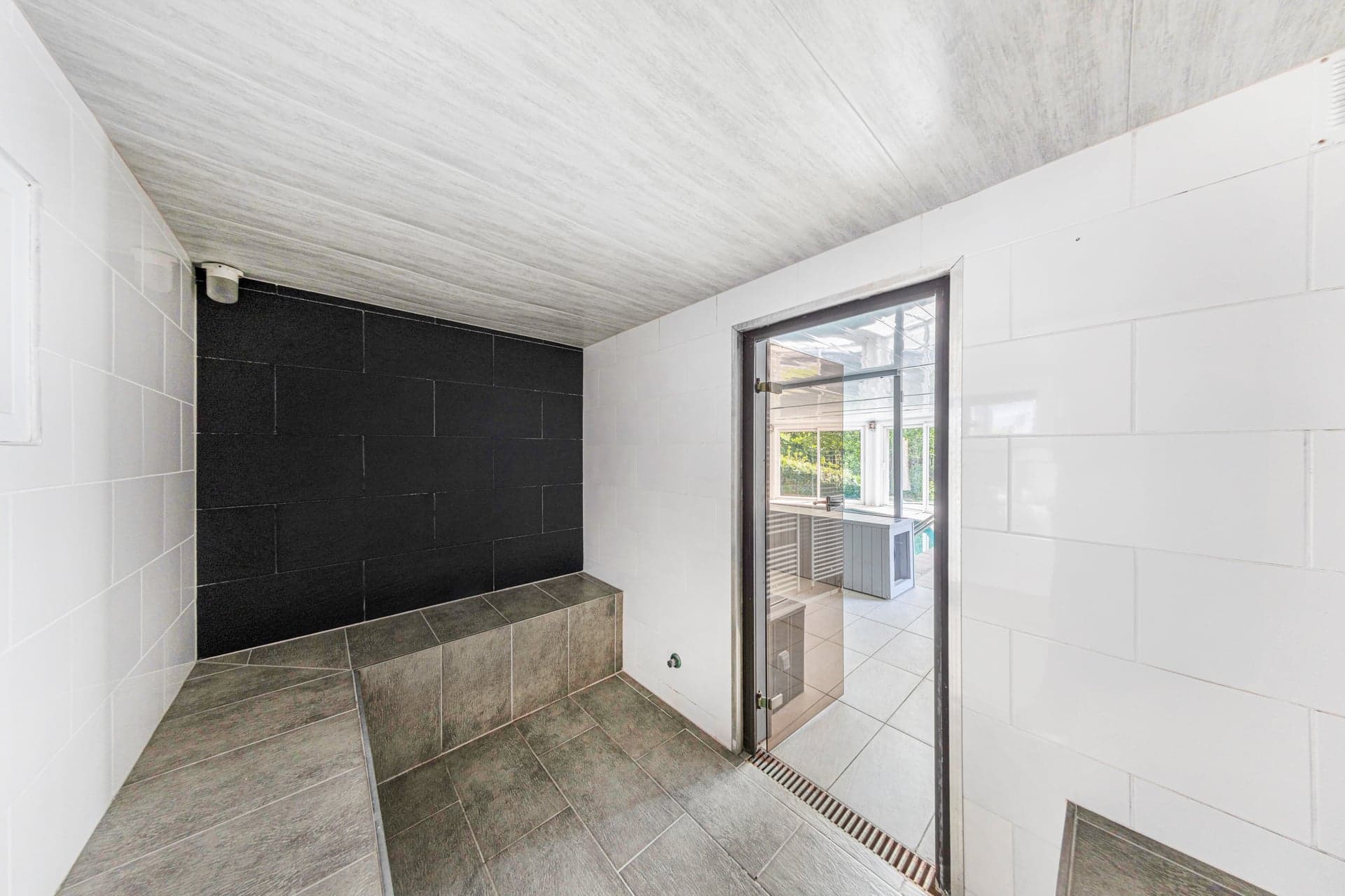 Hammam du gîte Gentiane carrelé noir et blanc avec banc et porte vitrée vers l'espace piscine (gîte groupe avec spa, Alsace)