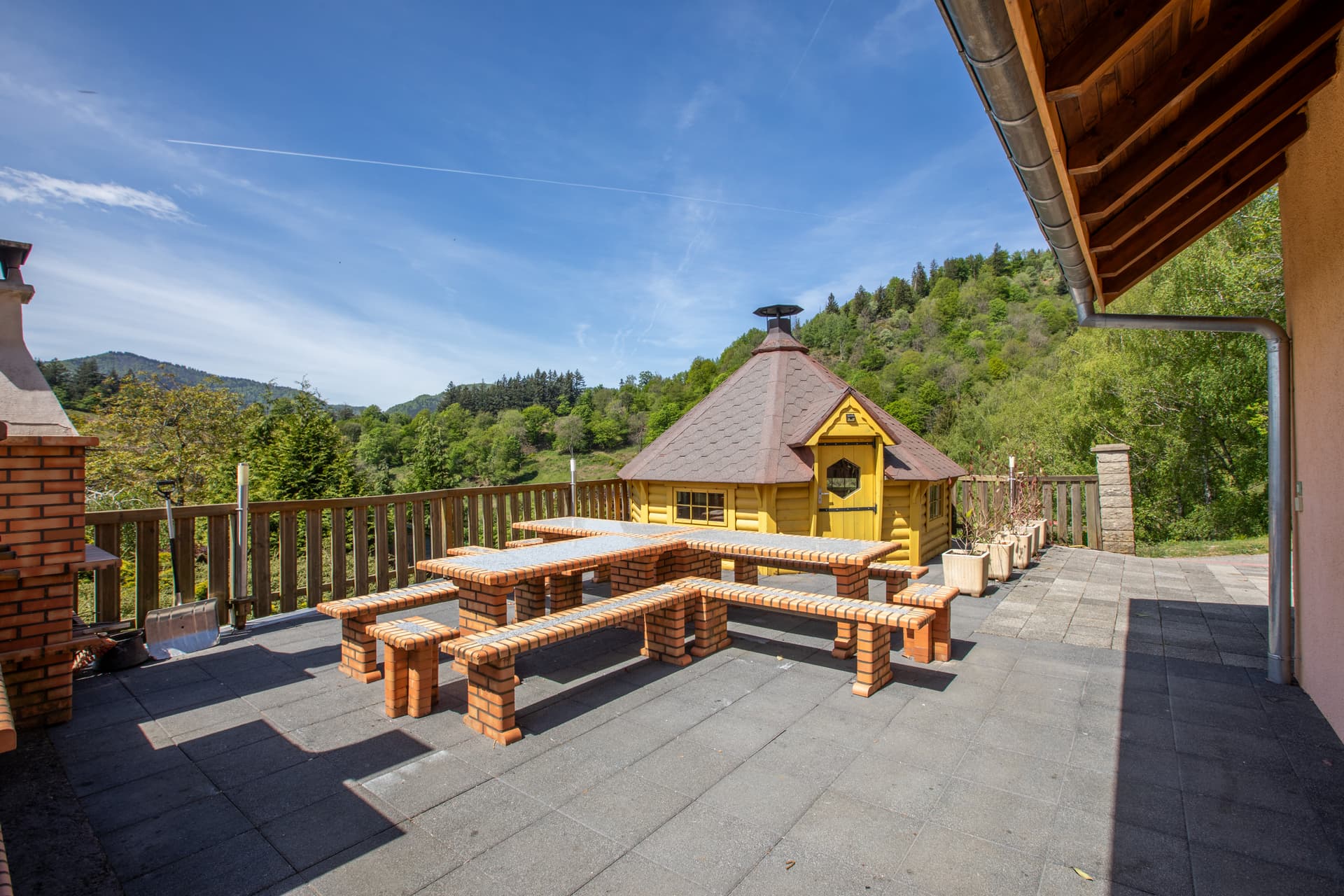 Kota grill finlandais du gîte Jonquille entouré de tables, vue sur les collines vosgiennes