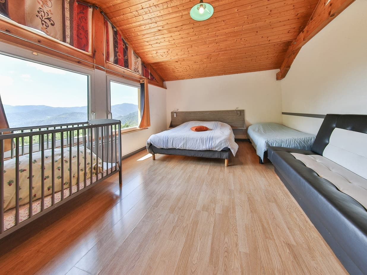 Chambre du Domaine du Gomm avec plafond bois et vue panoramique sur la vallée vosgienne